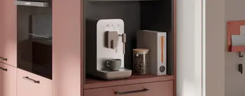 Detailansicht einer modernen Küche mit eingebauter Kaffeemaschine, Glasbehälter mit Kaffeebohnen und Deko. Warmes Farbkonzept in Rosé-Tönen mit eleganten Griffen und harmonischem Küchendesign.